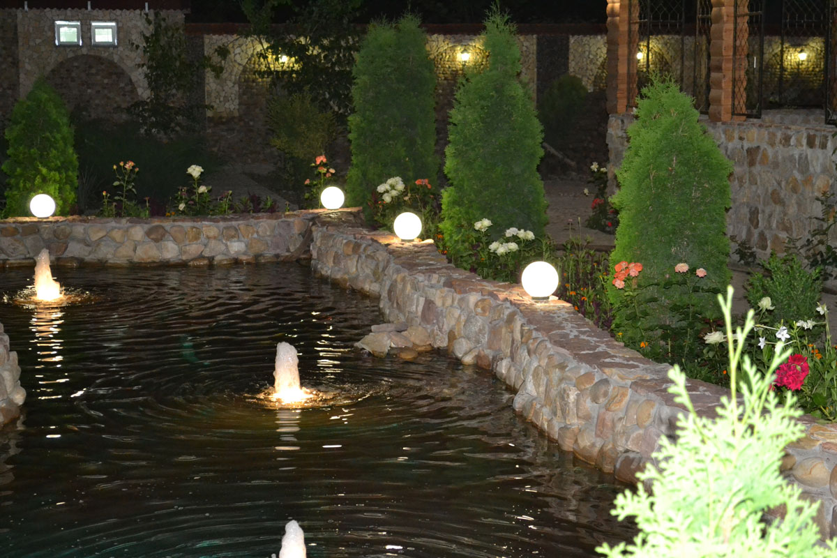 An awesome stone wall fountain surrounded with lights and plants