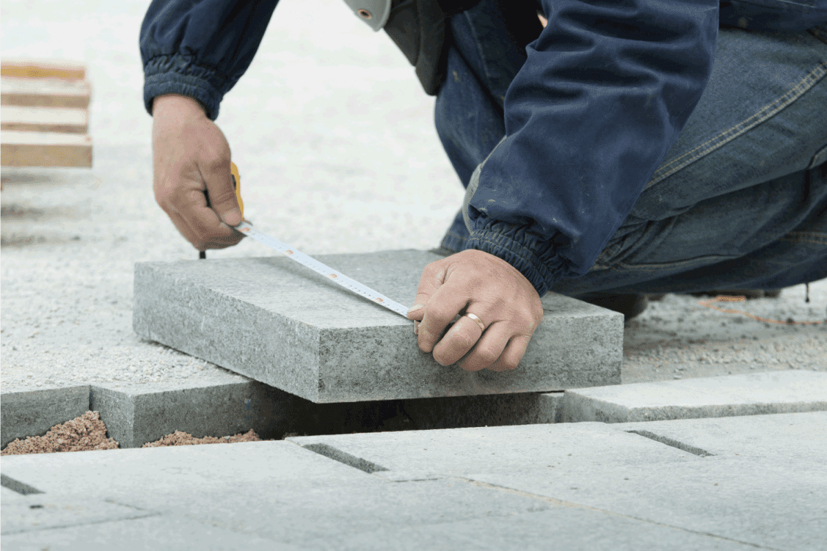 Construction worker measuring flagstone and preparing for cutting to fit in pavement