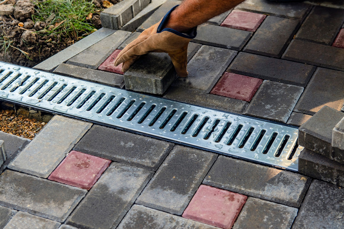 Landscaper placing gray and red paver bricks for the patio drain