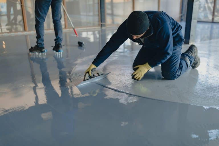 The worker applies gray epoxy resin to the new floor - Can Epoxy Be Used On Outdoor Patio