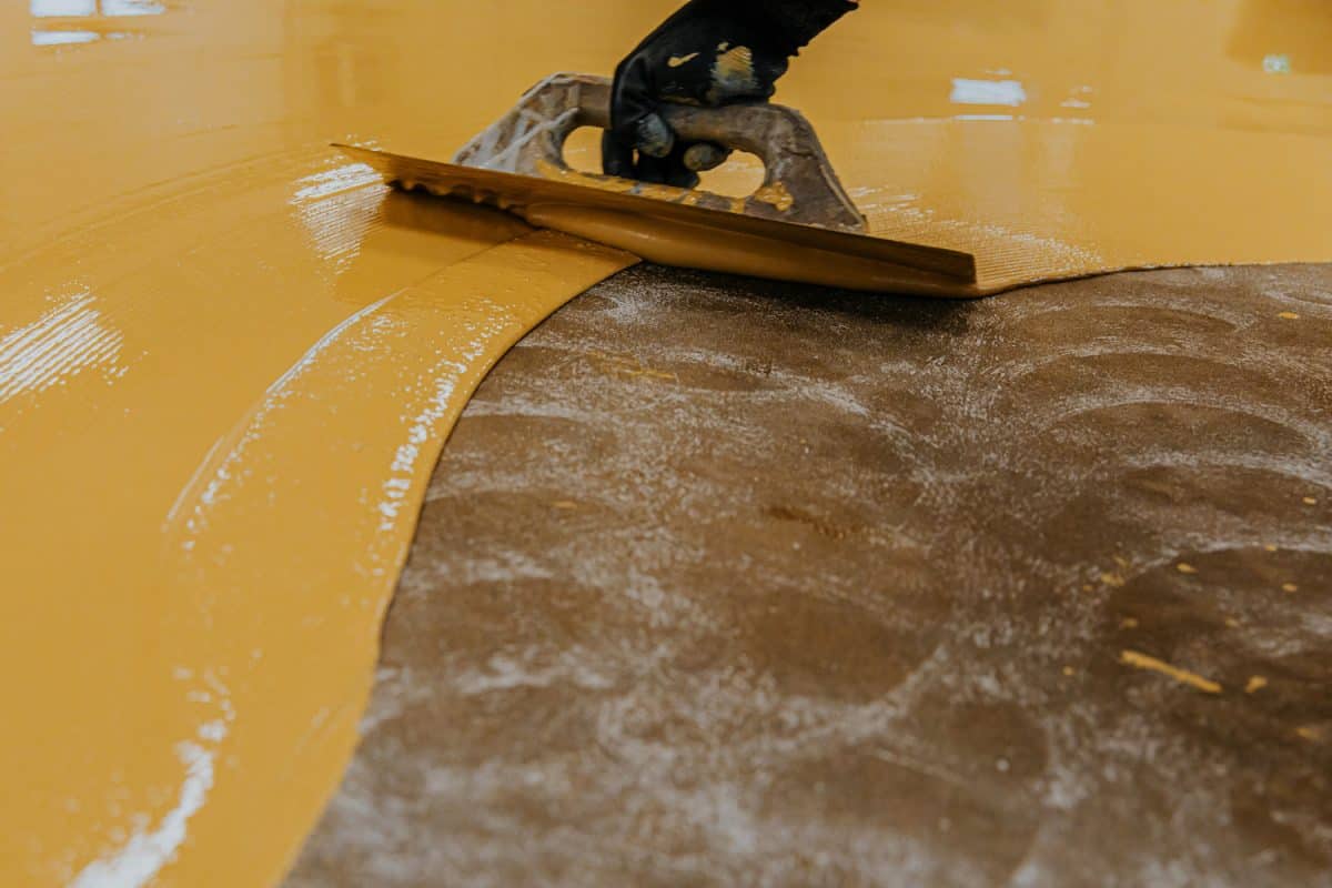 Worker, coating floor with self-leveling epoxy resin in industrial workshop. 