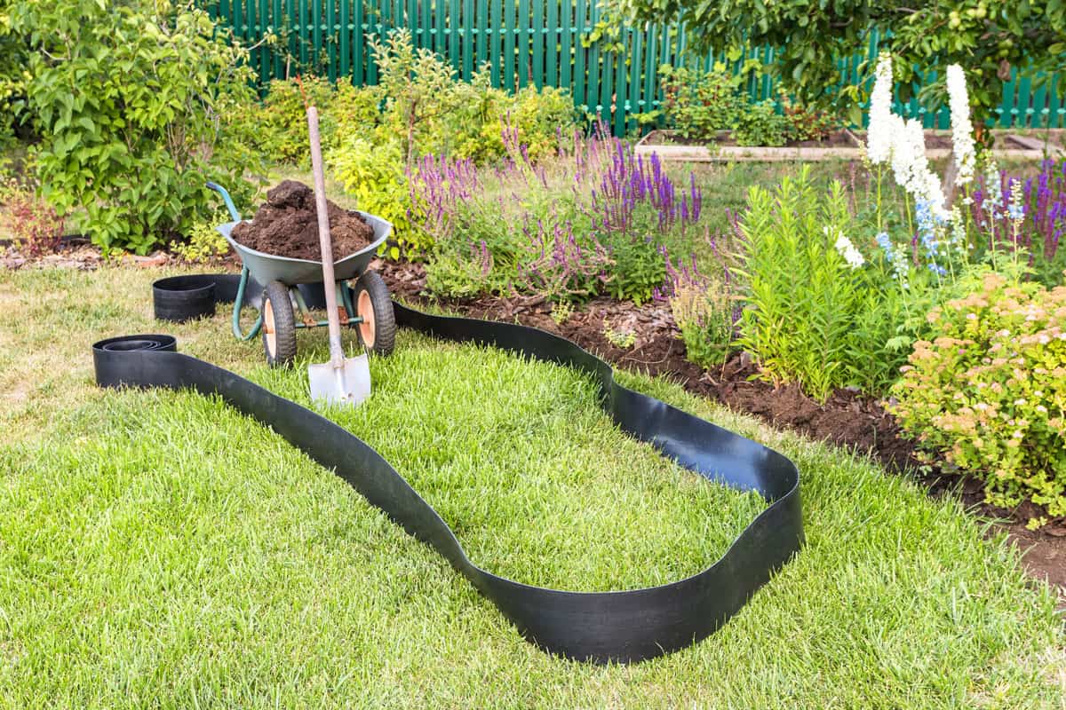 photo of a wheel borrow with soil inside, shovel on side, plastic landscaping edge on the ground